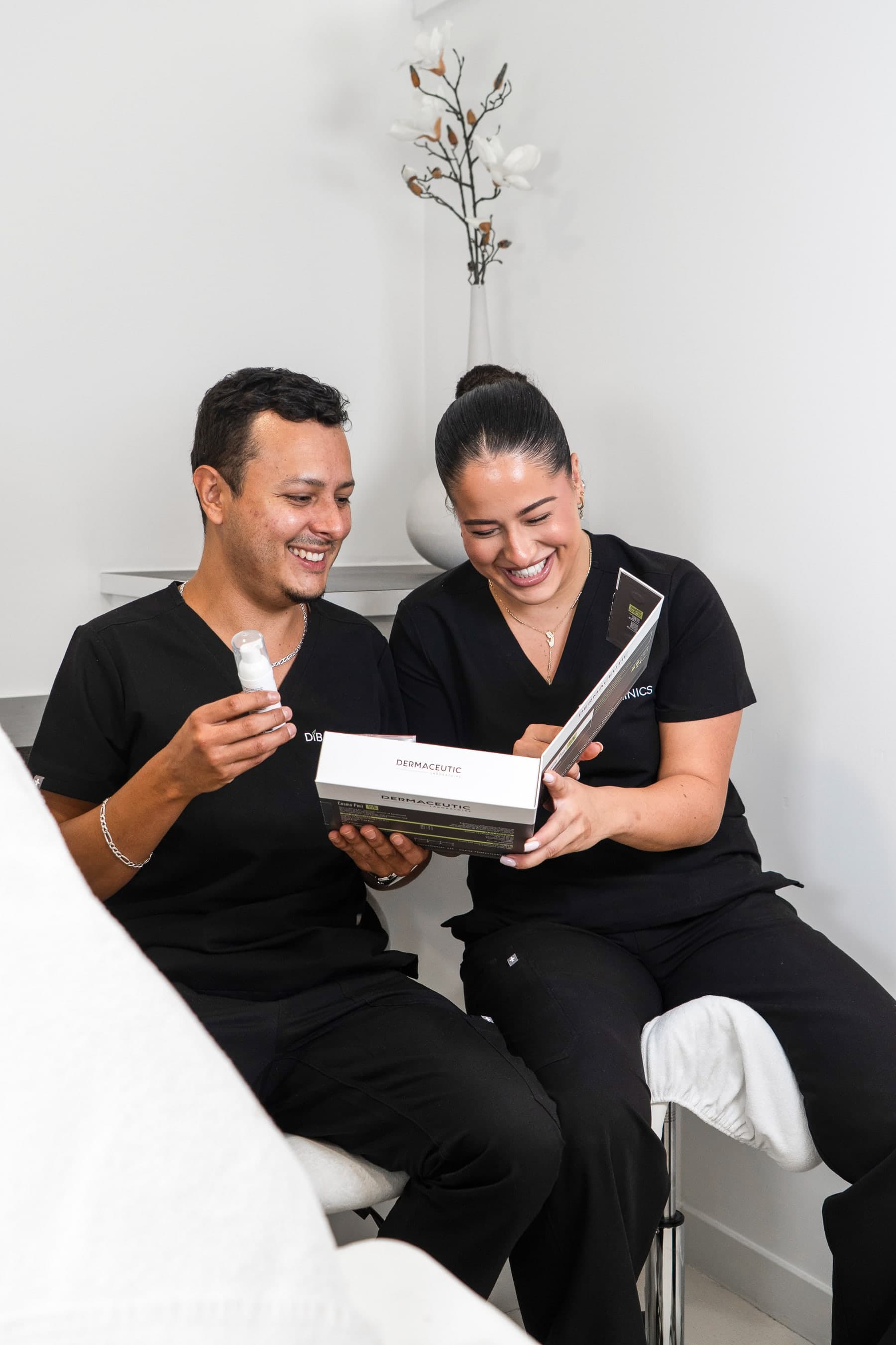 Twee behandelaars van Diba Clinics bekijken samen een doos van Dermaceutic en een flesje serum